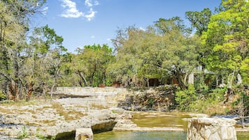 A natural landscape with a rocky water body, surrounded by trees and stone structures.