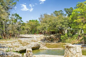 Paisaje natural con una masa de agua rocosa, rodeado de árboles y estructuras de piedra.