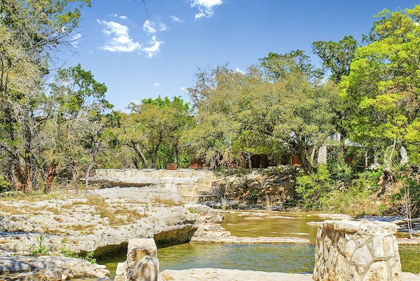 Paisaje natural con una masa de agua rocosa, rodeado de árboles y estructuras de piedra.