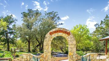 A stone archway with a sign, surrounded by trees and a pathway.