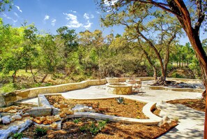 Un jardin aménagé avec des allées en pierre, des espaces de repos et une grande variété d’arbres.