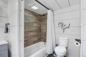 Un baño con pared de madera, bañera blanca, inodoro y cortina de ducha.