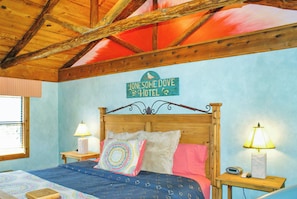 Un dormitorio con techo de madera, una cama con ropa de cama estampada, dos mesitas de noche con lámparas, y un cartel sobre la cama que dice 'Lonesome Dove Hotel'.