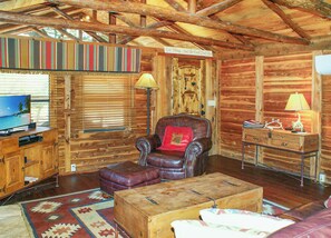 L’intérieur chaleureux d’un chalet avec un fauteuil en cuir, une table basse en bois et un téléviseur posé sur une commode en bois.