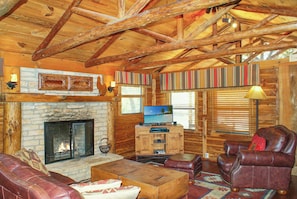 A log cabin interior with a stone fireplace, leather furniture, and a television. - Charming Creekside Cabin w/ Hot Tub, Fire Pit & Natural Rock Waterfalls (Wimberley)