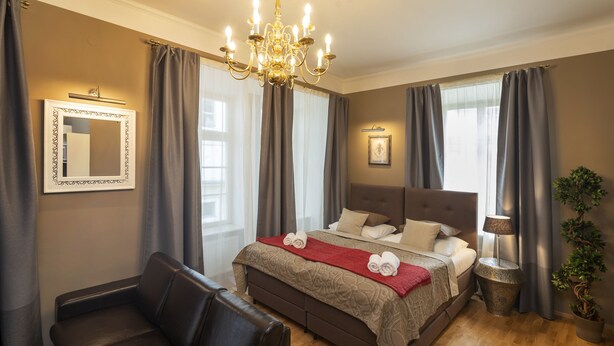 A bedroom with a large bed, a leather sofa, a chandelier, and a potted plant. - OLD TOWN - STUDIO MICHALSKA max 4 pers (Prague 1)