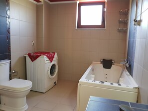 Een badkamer met toilet, wasmachine en bad.