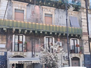 A building with a storefront labeled "MALANNATA" and multiple balconies with potted plants.