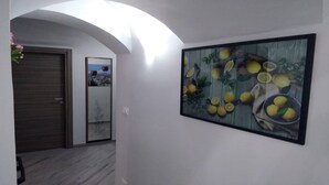 Un pasillo con un cuadro enmarcado de limones y una puerta que ofrece vistas a un paisaje urbano.