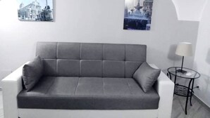 Una sala de estar moderna con un sofá gris, una mesita redonda con una lámpara y dos cuadros en la pared.