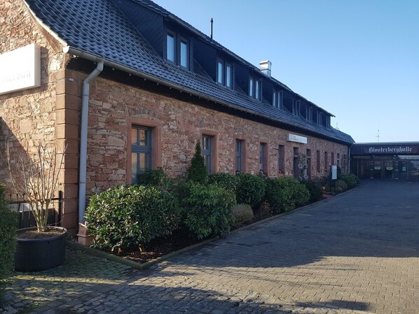 A stone building with a tiled roof, a sign reading "Hotel", and a paved entrance.