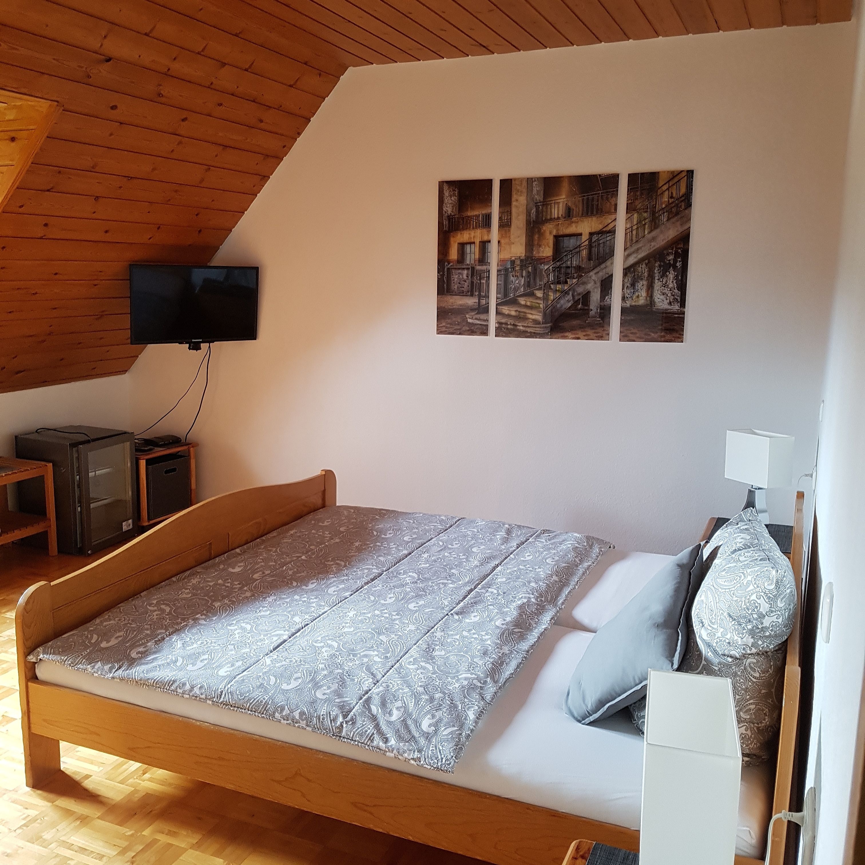 A bedroom with a wooden bed, a TV on a stand, a small table, and a wall-mounted shelf.