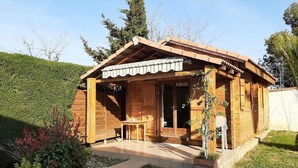 A wooden cabin with a covered porch, a small table, and a potted plant. - Two-bedroom apartment in the heights of Nice: Small chalet with private garden. (Nice)