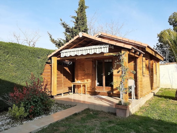 A wooden cabin with a covered porch, a small table, and a potted plant.