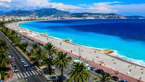 A coastal road with palm trees, a beach, and a clear blue sea. - Two-bedroom apartment in the heights of Nice: Small chalet with private garden. (Nice)