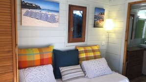 A bedroom with a bed, pillows, a mirror, and two wall-mounted pictures of a beach and a coastal town. - Two-bedroom apartment in the heights of Nice: Small chalet with private garden. (Nice)