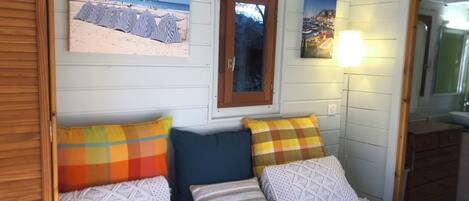 Une chambre à coucher avec un lit, des oreillers, un miroir et deux tableaux accrochés au mur représentant une plage et une ville côtière.