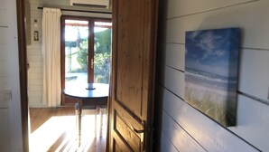 A room with a wooden door, a small table, and a view of greenery outside. - Two-bedroom apartment in the heights of Nice: Small chalet with private garden. (Nice)