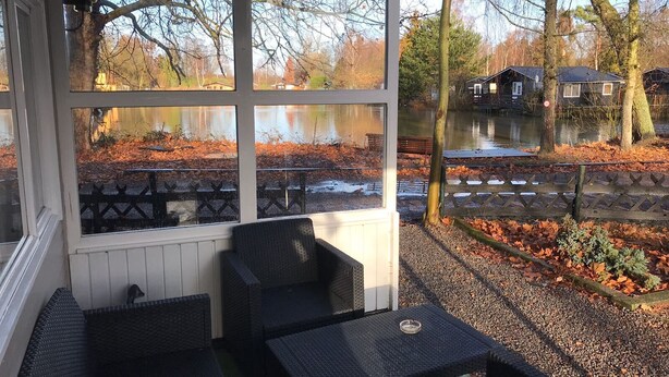 A covered outdoor seating area with a view of a lake and autumn foliage.