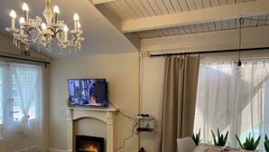 A living room with a fireplace, a television, a chandelier, a dining table, and potted plants.
