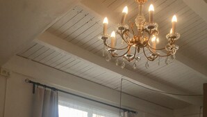 A dining area with a white table and chairs, a chandelier, and a kitchen in the background.
