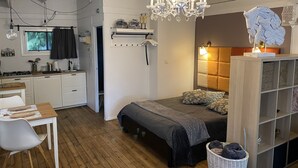 A compact bedroom with a bed, bedside table, and a nightstand. A chandelier hangs from the ceiling, and a small window provides natural light.