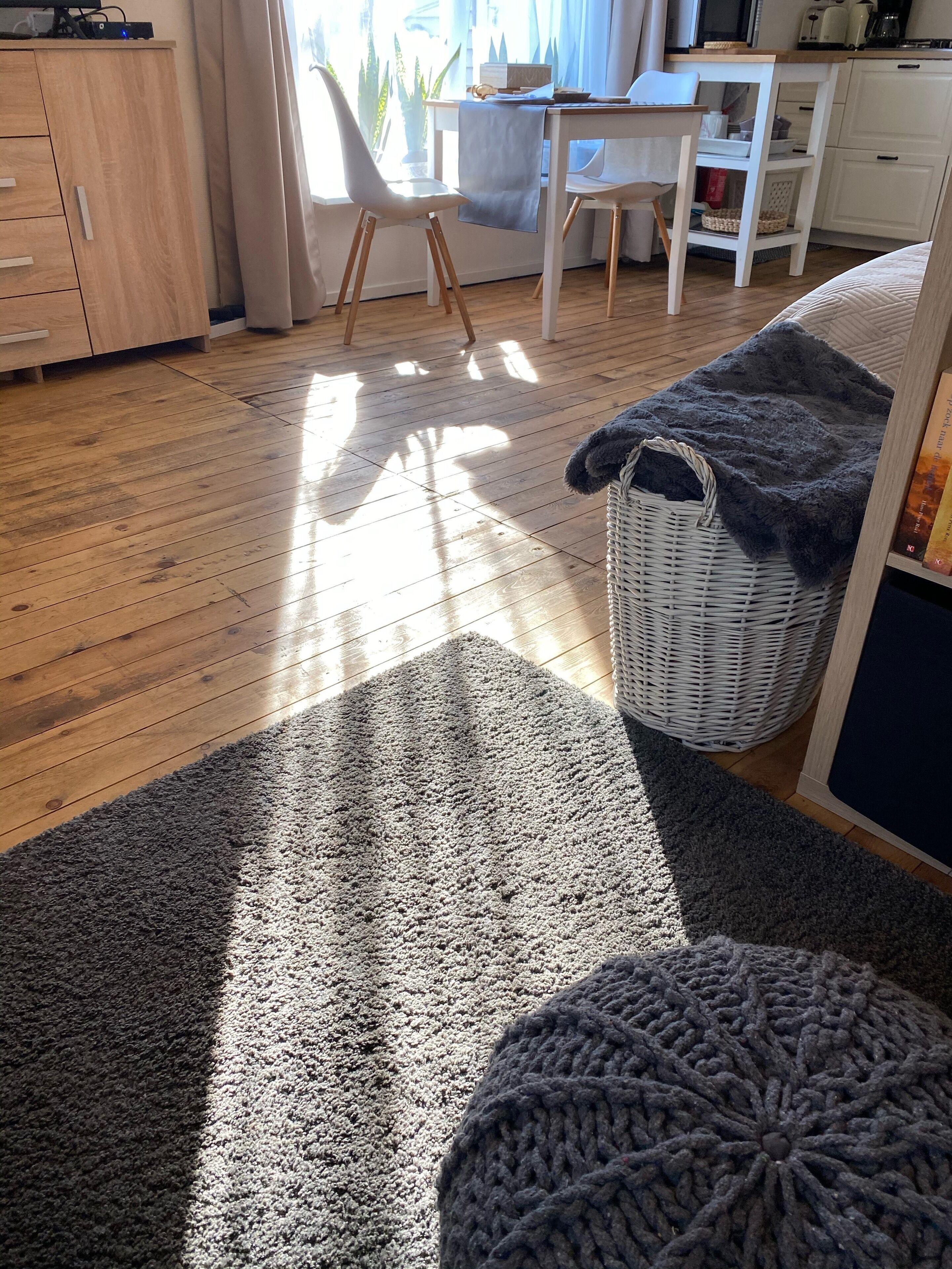 A room with a wooden floor, a grey carpet, a wicker basket, and a white chair.