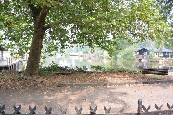 A lakeside view with a wooden bench, a tree, and a dock with cabins in the background.