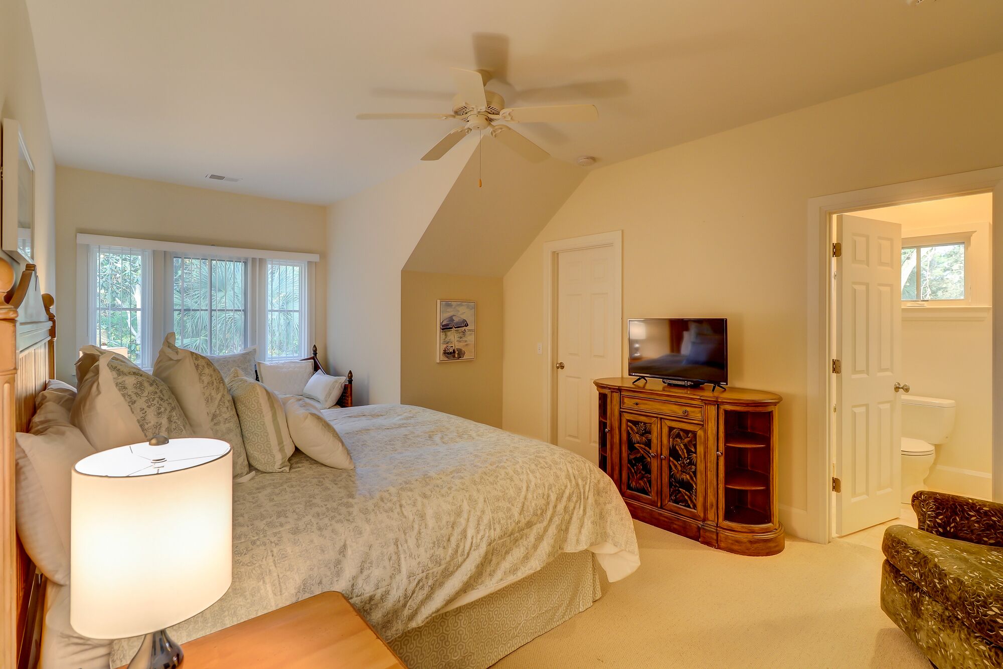 A bedroom with a bed, a ceiling fan, a TV, and a wooden cabinet.
