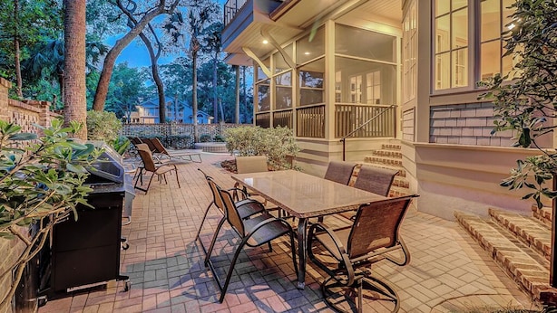 Een terras buiten met een eettafel en stoelen, omgeven door planten en een barbecue.