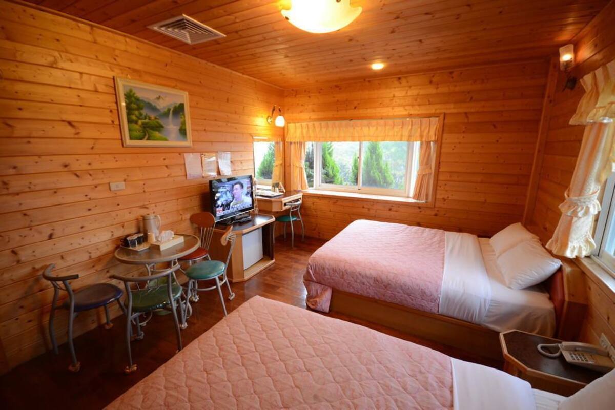 Ein gemütliches Cabin-Zimmer mit zwei Betten, einem Schreibtisch mit Computer, einem Fernseher und einem Fenster mit Vorhängen.