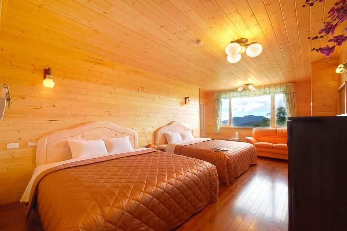 Ein gemütliches Blockhausszimmer mit zwei Betten, Holzwänden, einem Fenster mit Bergblick und einer kleinen orangefarbenen Couch.