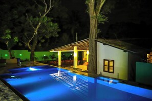 Un área de piscina con un pequeño edificio, rodeado de árboles.