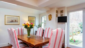 A dining area with a wooden table, striped chairs, a vase of flowers, a framed picture, and a television on the wall. - Rose-Tinted Charm, by Veeve (London)