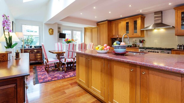 A spacious kitchen with wooden cabinets, a granite countertop, and a large island with fruit. - Rose-Tinted Charm, by Veeve (London)