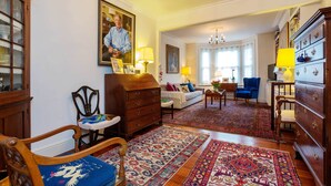 A spacious living room with a large wooden cabinet, a blue armchair, a sofa, and a patterned rug. - Rose-Tinted Charm, by Veeve (London)