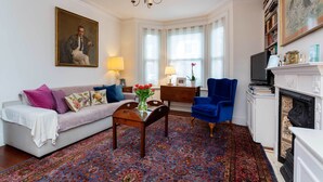 A living room with a sofa, armchair, coffee table, and a fireplace. - Rose-Tinted Charm, by Veeve (London)