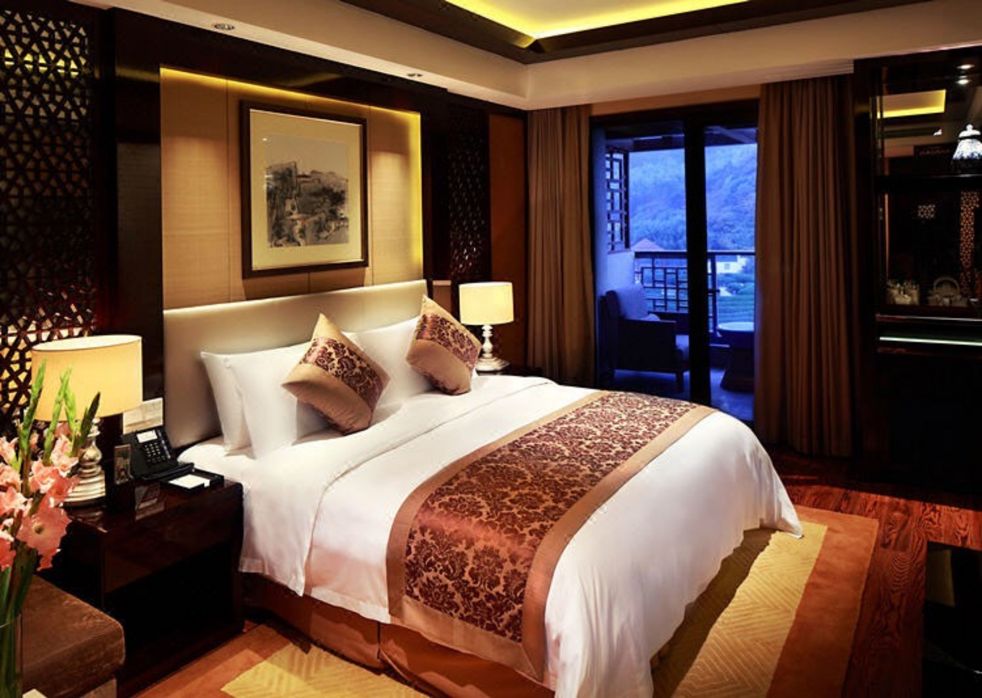 A hotel room with a large bed, a desk with a lamp, a phone, and a view of the outdoors.