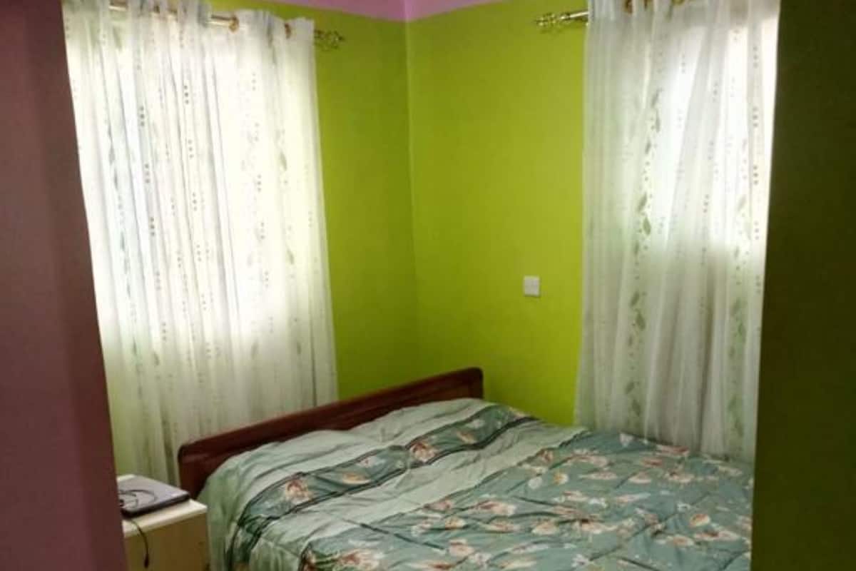 Un dormitorio con cama, cortinas, escritorio y piso de baldosas.