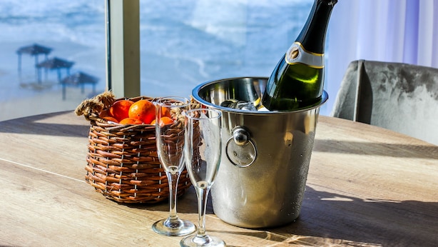 Une table sur laquelle se trouve un seau en métal contenant une bouteille de champagne, deux verres et un panier en osier rempli d’oranges.