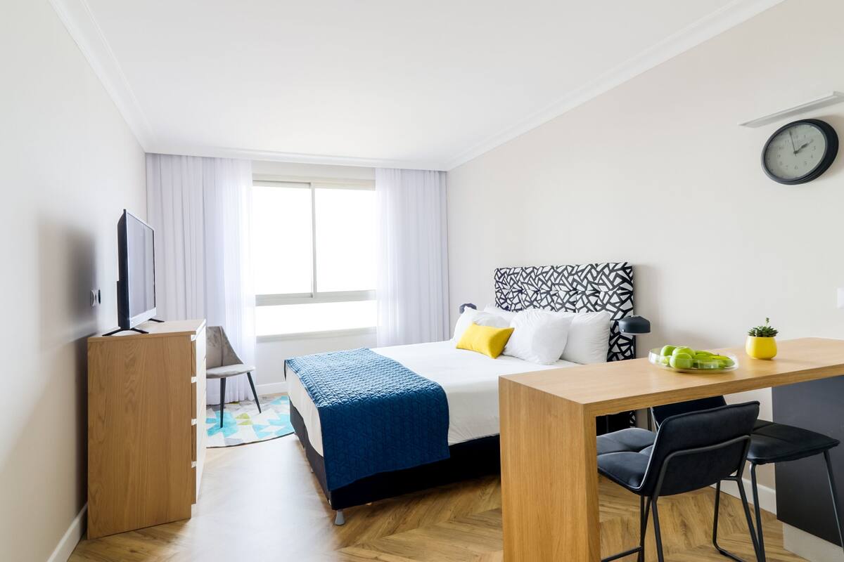Une chambre d’hôtel moderne équipée d’un lit, d’un bureau, d’une chaise, d’une télévision et d’une horloge murale.
