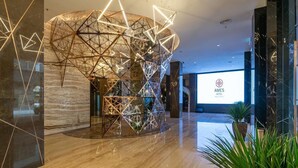 Un moderno vestíbulo de hotel con una instalación de luces geométricas, suelo de mármol y un letrero visible del HOTEL AMES.