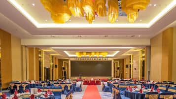 A banquet hall with rows of tables, red carpet, and golden chandeliers.