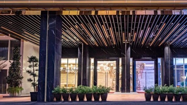 Una entrada de hotel moderna con un paseo techado, amplias ventanas y plantas en macetas.