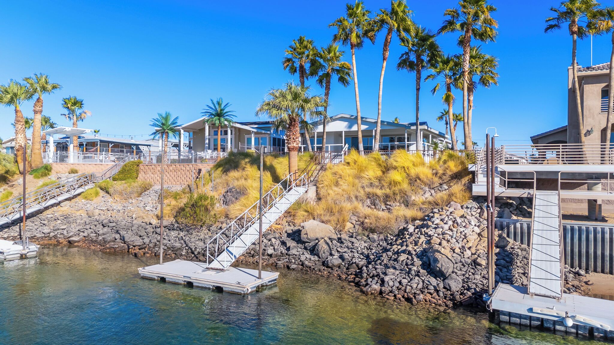 A coastal hotel with a rocky shoreline, palm trees, and a clear blue sky.