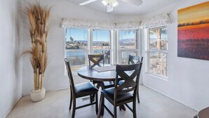 A dining area with a round table, four chairs, a ceiling fan, and large windows offering a view of the landscape.