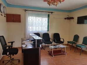 A room with a desk, chairs, a television, and a window with a curtain. - Sanfields Lodwar Camp (Lodwar)