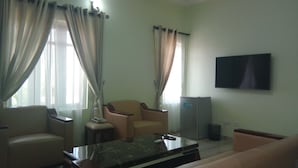 Ein Wohnzimmer mit einer Couch, einem Sessel, einem Couchtisch, einem Fernseher und einem kleinen Tisch mit einer Lampe.