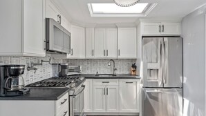 Une cuisine moderne avec des armoires blanches, des appareils en acier inoxydable, un puits de lumière et un dosseret décoratif.