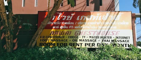 A sign for a guesthouse offering amenities like air conditioner, fridge, TV, water heater, internet, foot massage, oil massage, and Thai massage.